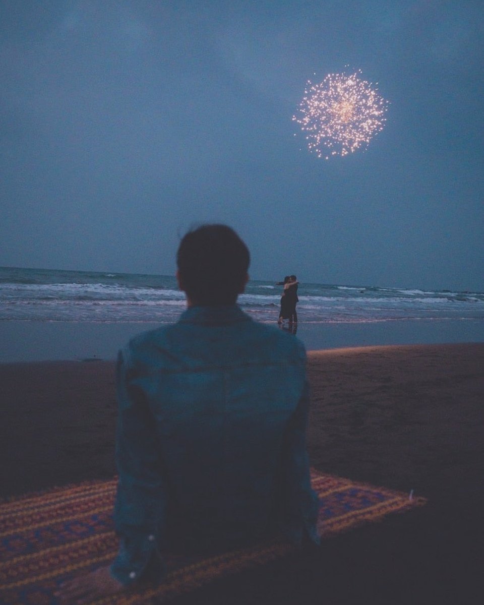 Sitting on a woven rug as fireworks light the night sea