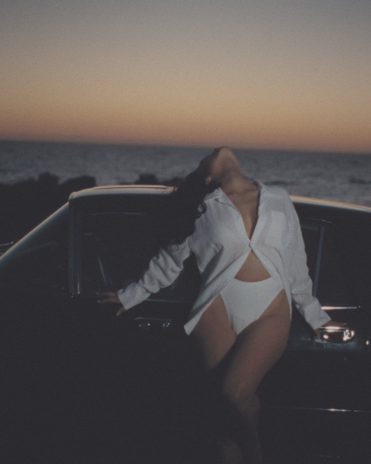 Leaning back against a car by the sea at dusk